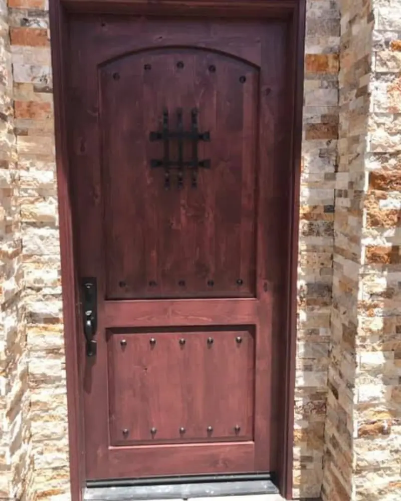 Rustic stained arch-top entry door with iron speakeasy grille and stone surround